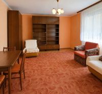 A living room in a family house with an orange carpet and wooden furniture.