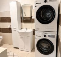 Washing machine and dryer in the bathroom of a family house with marble tiles and a mirror.