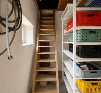 Wooden stairs, shelves with boxes, and hoses in the basement area of the family house.