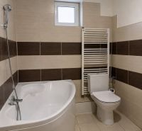 A bathroom in a family house with a bathtub, toilet, and radiator, tiles with a brown decor.