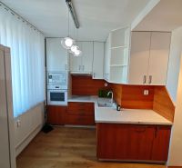 A kitchen in a studio apartment with built-in appliances and a wooden decor floor.
