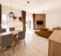 A spacious living room in a three-room apartment with a wooden decor floor and a dining area.