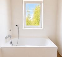 Bathroom with a bathtub and a window, white tiles, floor with wood decor in a 3-room apartment.