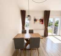Dining area in a 3-room apartment with a wood-patterned floor and a large window.