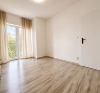 A bright room with a wood-patterned floor and curtains in a three-room apartment.