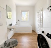 A bathroom in a 3-room apartment with a bathtub, washing machine, and a floor with a wooden decor.