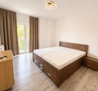 A bright bedroom with a bed, a nightstand, and a wooden decor floor in a 3-room apartment.