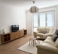 A bright living room of a 3-room apartment with sofas, a TV, and a wooden-decor floor.