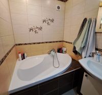 A bathroom with a corner bathtub and subtle tiles in a 3-room apartment.