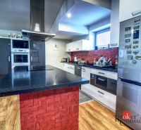 A kitchen in a family house with an island, red tiles, and a wooden decor floor.