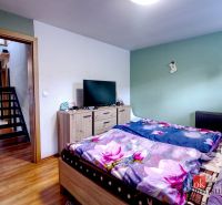 A bedroom in a family house with a television, a dresser, and a bed with floral bedding.
