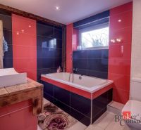 Bathroom with red and black tiles, a bathtub, and a wooden sink table in a family house.
