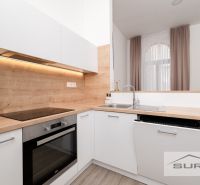 A kitchen in a 2-room apartment with a wooden decor floor and white cabinets.
