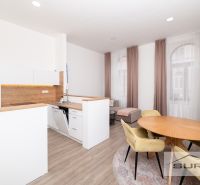 A kitchen in a 2-room apartment with a wood-patterned floor, a dining table, and windows with curtains.