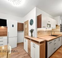 A kitchen in a 2-room apartment with a white refrigerator, wooden decor on the floor and walls.