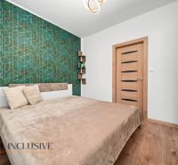 A bedroom with green geometric wallpaper, a bed, and a wooden decor floor in a two-room apartment.
