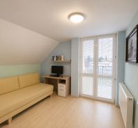 A room with a sofa, a computer desk, and a wooden-patterned floor in a family house.