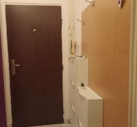 Entrance hallway in a one-room apartment with a coat rack, white cabinets, and tiles.