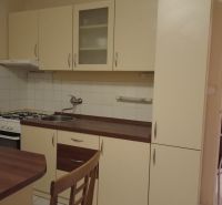 A kitchen in a one-room apartment with white cabinets and wooden decor.