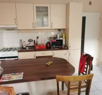 A kitchen in a studio apartment with a stove, wooden decor, and white cabinets.