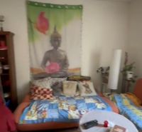 A room in a family house with a colorful blanket and a tapestry with Buddha on the wall.