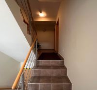 A hallway with a staircase and railing in a family house, floor made of ceramic tiles.