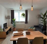 Living room in a family house with wood-patterned flooring, plants, and wall lights.