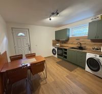 A kitchen in a family house with a kitchen unit, a washing machine, a table, and a floor with a wooden decor.