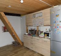 Interior of a cabin with a wooden ceiling, kitchen counter, and staircase, floor with wooden decor.