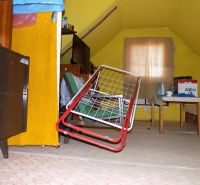 Interior of a cottage with a drying rack, table, and yellow walls. There is an attic and cabinets.