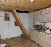 The interior of the cottage with stairs, a kitchen unit, and a wooden decor floor.