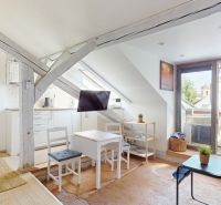 Attic studio apartment with wooden beams, a dining table, and a view of the rooftops.