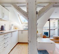 Kitchen corner and living room in a studio apartment with light furniture and wooden decor.