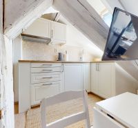 A kitchen unit in the attic with a TV, light cabinets, and a beam.