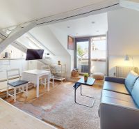 Attic space of a one-room apartment with a kitchen, sofa, and a view from the window.