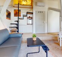 Bright 1-room apartment with wooden beams, a staircase to the upper floor, and a comfortable sofa.