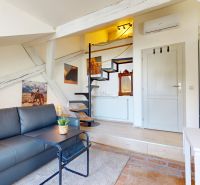 Attic studio apartment with a sofa, stairs, and paintings on the wall.