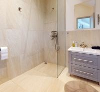 A bathroom in a studio apartment with a freestanding shower and a sink with a cabinet.
