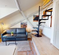 Attic studio apartment with a sofa, staircase, and wall decorations.