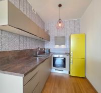 A kitchen in a studio apartment with a yellow refrigerator and a wood-patterned floor.