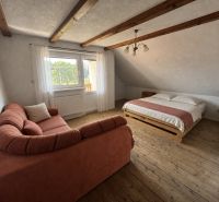 A bedroom in a family house with a wooden decor floor, a sofa, and a bed.