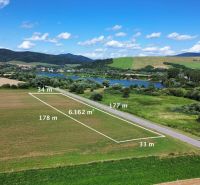 Plots - housing in Plaveč by the road, with a view of the surrounding countryside and water surface.