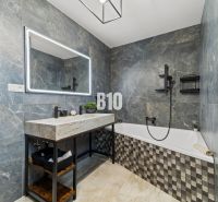 A bathroom in a family house with a bathtub, stone tiles, and a large mirror.