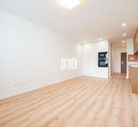 A bright kitchen with white cabinets and a wood-patterned floor in a three-room apartment.