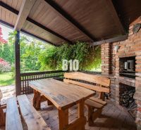 Terrace of a family house in Nitra with wooden seating, a grill, and greenery in the surroundings.