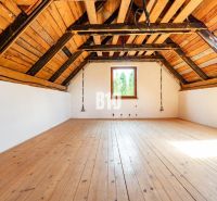 Attic room with wood-decor flooring in a family house, illuminated by a large window.
