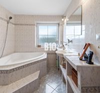 A bathroom in a family house with a corner bathtub and a window, light tiles.