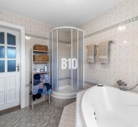 A bathroom in a family house with a bathtub, shower, and a towel shelf.