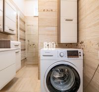 A bathroom in a family house with a washing machine and light-colored tiles.