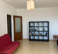 A room in a one-room apartment with a shelving system, a red sofa, and a wooden decor floor.